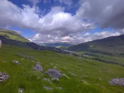 a green grassy hill with mountains in the background at Holiday Home Benmore Farm House in Stirling mit Bergblick by Interhome in Crianlarich