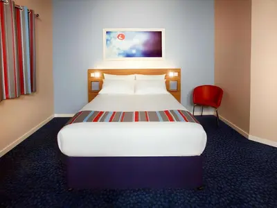 a bedroom with a large bed and a red chair at Travelodge Edinburgh Dreghorn in Edinburgh