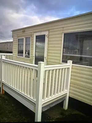 a mobile home with a white railing on a porch at Sandylands caravan park in Stevenston
