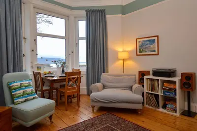 a living room with a chair and a table and a window at Montford Shore in Rothesay
