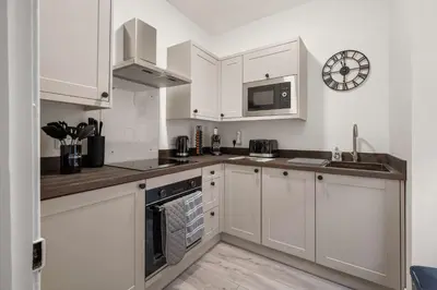 a kitchen with white cabinets and a clock on the wall at Stylish 1BR Central Oban Retreat in Oban