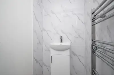 a bathroom with a sink and a white marble wall at Vacant Nests Unique 4BR home The Muirhouse in Motherwell