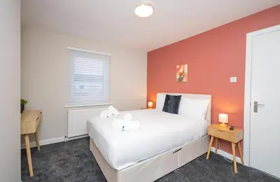 a bedroom with a white bed and an orange wall at Vacant Nests Unique 4BR home The Muirhouse in Motherwell