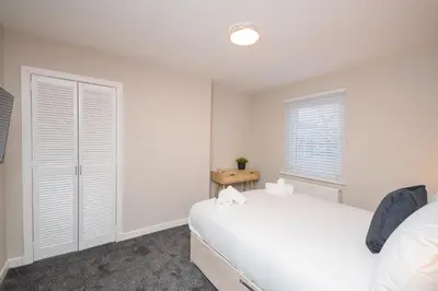 a white bedroom with a bed and a window at Vacant Nests Unique 4BR home The Muirhouse in Motherwell