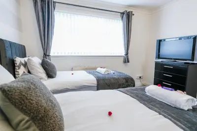 two beds in a room with a tv and a window at Jake's House in Airdrie