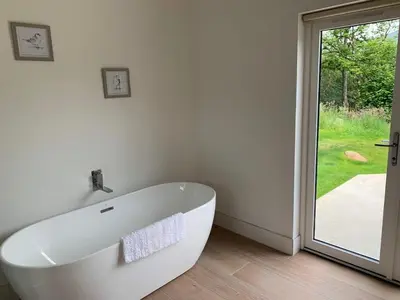 a white bath tub in a bathroom with a sliding glass door at The Tractor Shed- Elevated Hot Tub with Loch Views