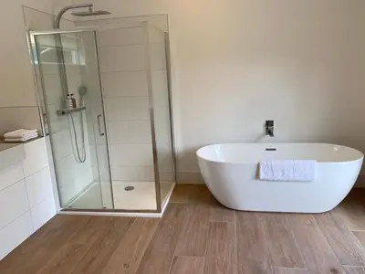 a bathroom with a white tub and a glass shower at The Tractor Shed- Elevated Hot Tub with Loch Views