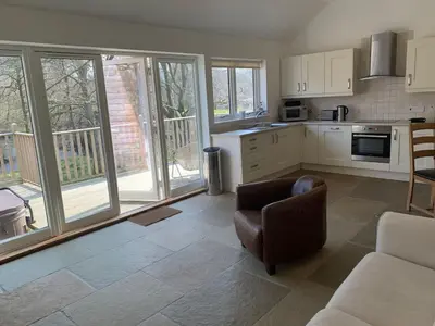a living room with a couch and a kitchen with windows at Garth Cottage - Riverside with Private Hot Tub in Killin