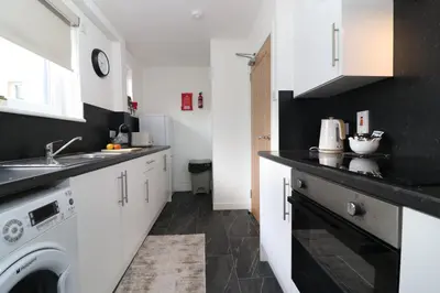 a kitchen with white cabinets and a washer and dryer at Signature Greenfield House in Wishaw