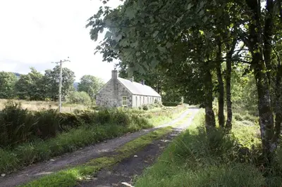 an old stone house in the middle of a dirt road at Clachandubh Cottage in Lochgilphead