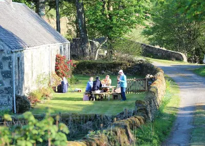 a group of people sitting at a picnic table in the grass at Clachandubh Cottage in Lochgilphead