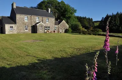 a large house on a grassy field with purple flowers at Finchairn Farmhouse in Lochgilphead