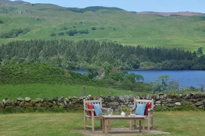 a table with two chairs sitting next to a lake at Finchairn Farmhouse in Lochgilphead