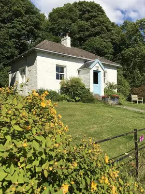 a small white house in a yard with flowers at South Lodge in Lochgilphead