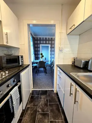 a kitchen with white cabinets and a dining room with a table at Bright and Cozy 3BR Home Near Hampden Park in Glasgow