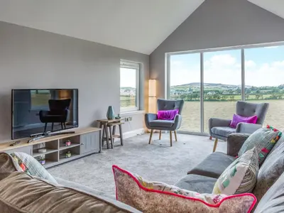 a living room with a couch and a tv and windows at A'chrannchuir in Blackwaterfoot