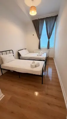 two beds in a room with a wooden floor at Acorn Spacious Stay Glasgow in Glasgow