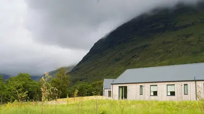 a building in a field next to a mountain at Auch - Cottages in Bridge of Orchy