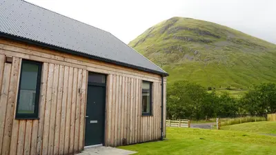 a wooden building with a mountain in the background at Auch - Cottages in Bridge of Orchy