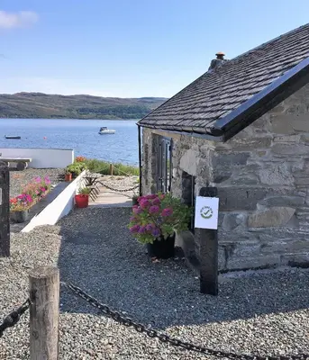 a stone building with a sign on it next to the water at Pier Cottage at Kames in Kames