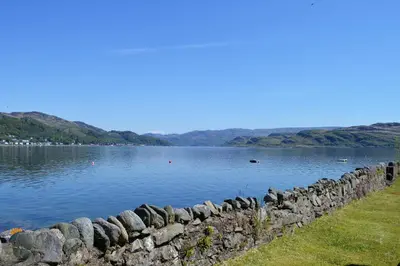 a large lake with a stone retaining wall and water at Pier Cottage at Kames in Kames