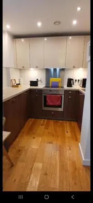 a kitchen with wooden floors and white cabinets and an oven at Stylish Clyde Riverfront Flat with Balcony Views in Glasgow