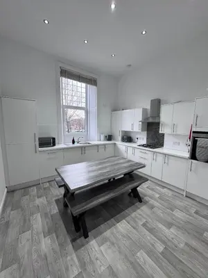 a large white kitchen with a wooden table in it at Station Road Apartment - Macaulay Letting in Dumbarton