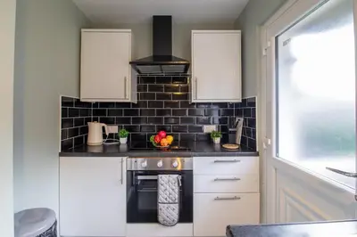 a kitchen with white cabinets and a black tile wall at Culzean House - 2 Bedrooms in Coatbridge in Coatbridge