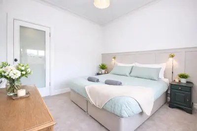 a white bedroom with a large bed and a table at Portside Apartment in Greenock