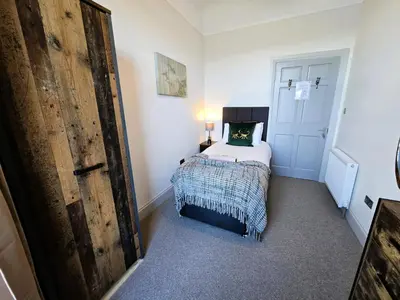 a small bedroom with a bed and a wooden door at Harbour View - Luxury Town Centre Property in Rothesay