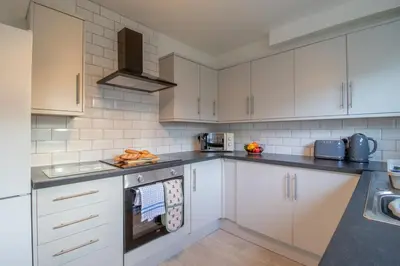 a kitchen with white cabinets and a stove top oven at Raeburn House- 3 Bedrooms, 2 Bathrooms in Hamilton in High Blantyre