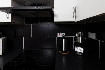 a kitchen with white cabinets and a black counter top at Central Cosy Apartment by Meadows 6 in Edinburgh