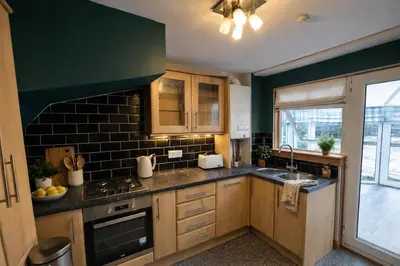 a kitchen with wooden cabinets and a green wall at Comfortable 3 Bed Home with Garden & Parking Stylish Family Contractor in Newton Mearns
