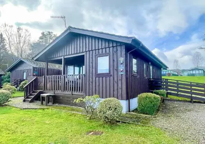 a small cabin with a porch and a fence at Heather Lodge with Hot Tub in Hunters Quay