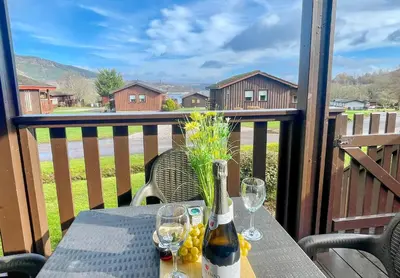 a table with a bottle of wine and glasses on a balcony at Heather Lodge with Hot Tub in Hunters Quay
