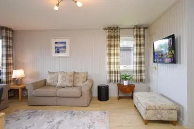 a living room with a couch and a tv at Heather Lodge with Hot Tub in Hunters Quay
