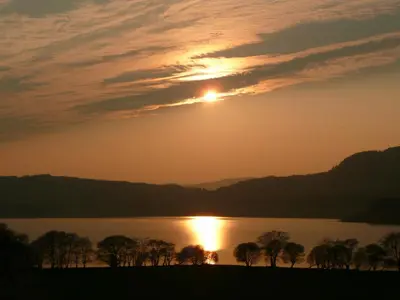 a sunset over a lake with trees in the foreground at Blarghour Farm Cottages in Ardchonnell