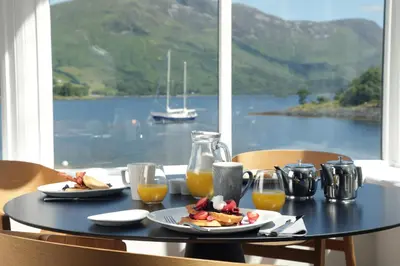 a table with food and orange juice and a view of the water at The Isles of Glencoe Hotel in Glencoe