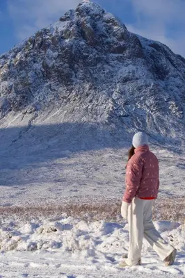 a woman walking in the snow in front of a mountain at RiverBeds - Luxury Wee Lodges with Hot Tubs in Glencoe