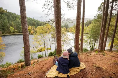 a group of people sitting on a hill overlooking a lake at RiverBeds - Luxury Wee Lodges with Hot Tubs in Glencoe