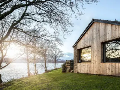 a wooden house on a hill next to a body of water at Carsaig in Port of Menteith