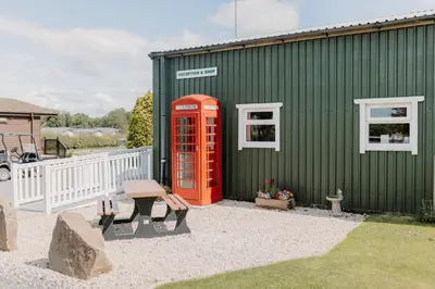 a green building with a red phone booth and a bench at Linwater Caravan Park - Luxury Lodges and Static Caravans near Edinburgh in Newbridge