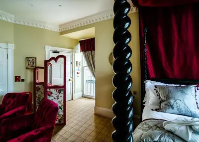 a room with a bed and a chair and a mirror at Crossbasket Castle, Hotel & Restaurant in High Blantyre
