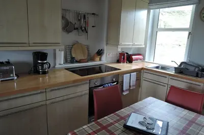 a kitchen with wooden cabinets and a table with red chairs at Tigh Beg Croft in Lerags