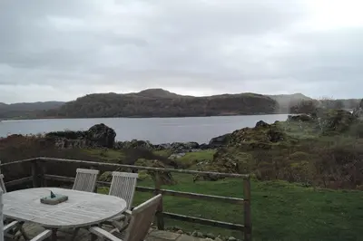 a table and chairs on a deck with a view of a lake at Tigh Beg Croft in Lerags
