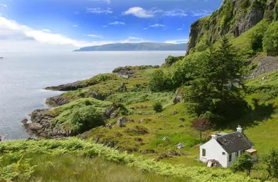 a small white house on a hill next to the ocean at Tigh Beg Croft in Lerags