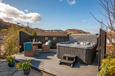 a hot tub and a table and chairs on a deck at Katie's Flat in Oban