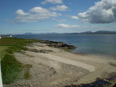 a beach with the ocean and a lighthouse in the distance at Port Charlotte Youth Hostel in Port Charlotte