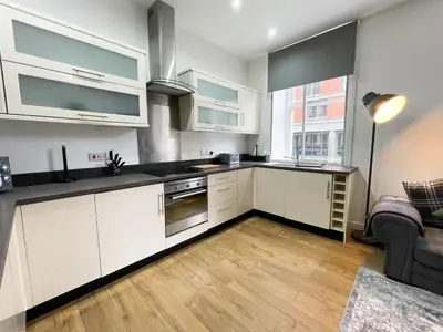 a kitchen with white cabinets and a living room at Exquisite 2BR Flat near Central Train Station in Glasgow