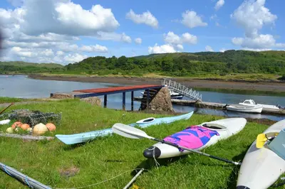 a group of kayaks sitting in the grass near a river at Oban Seil Farm in Clachan